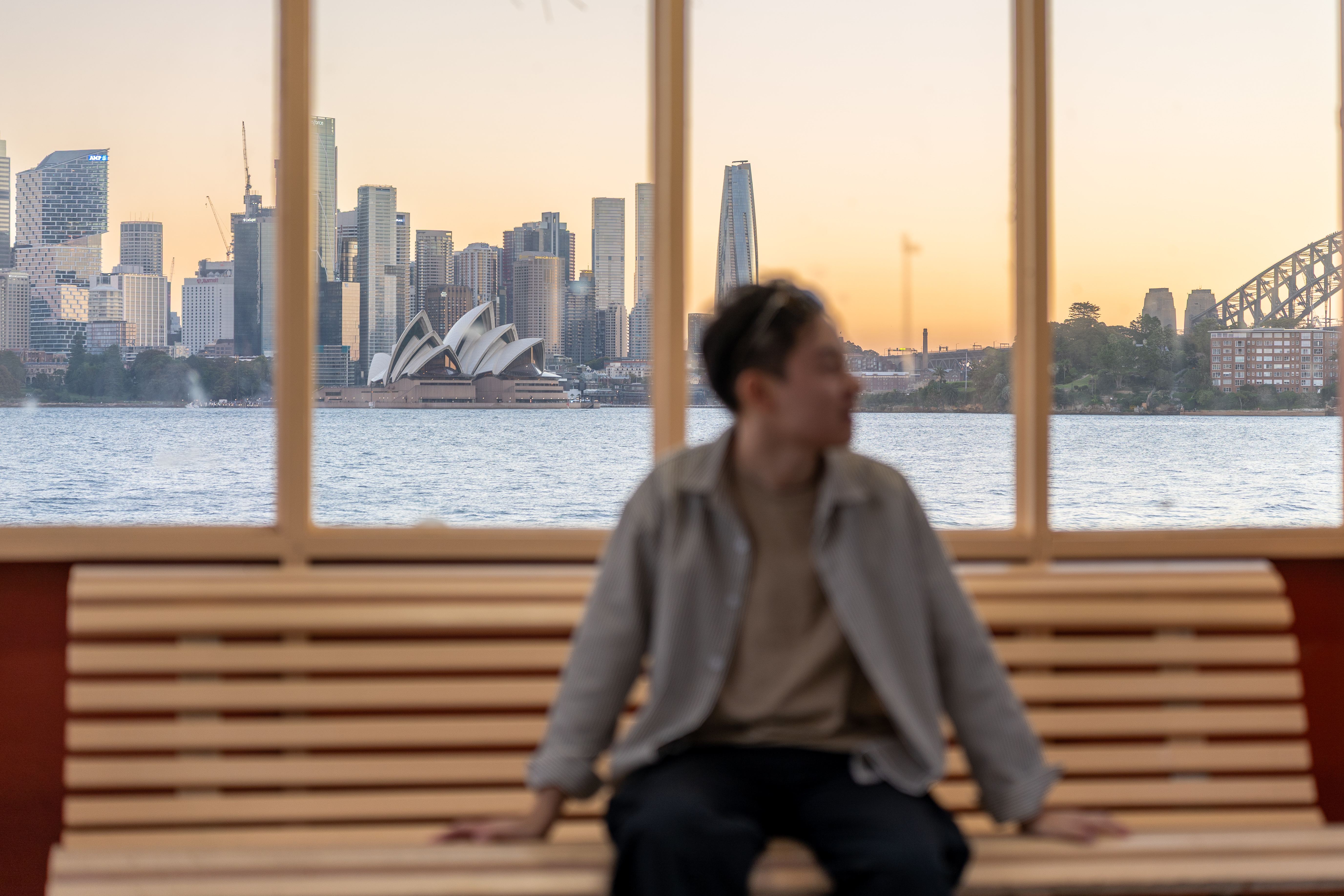 A figure on a Sydney ferry framed against the harbour, Opera House and Harbour Bridge at dusk
